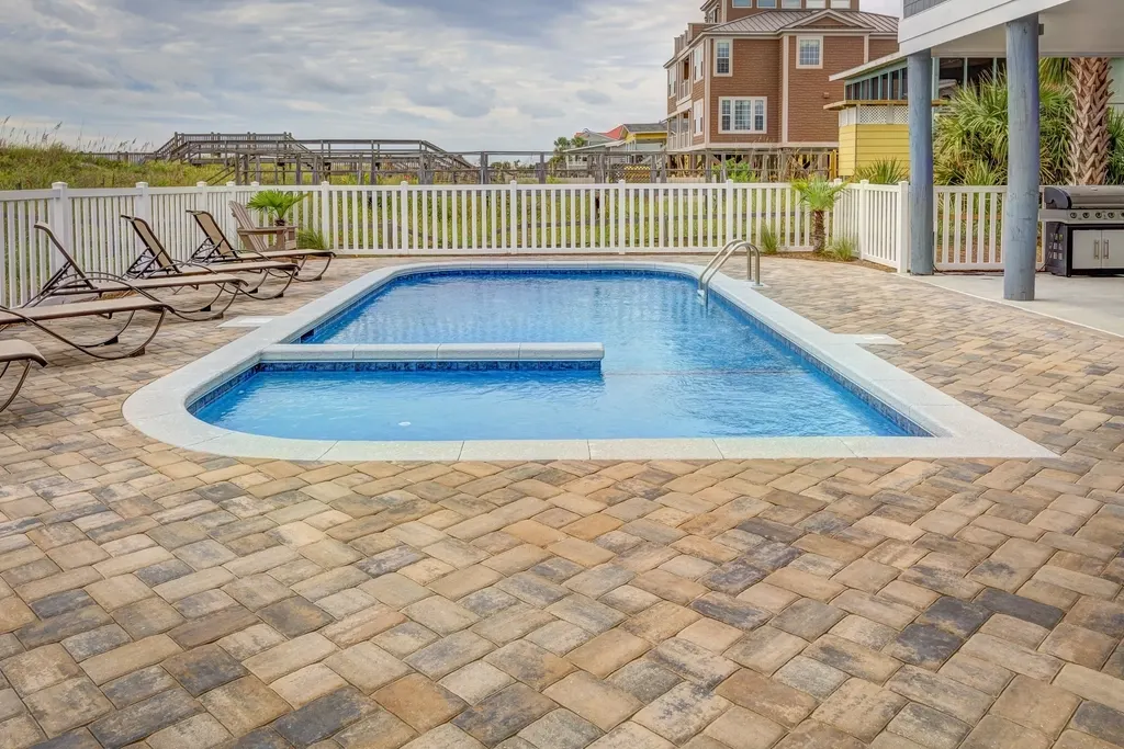 Tan and gray concrete paver deck around a rectangular pool with white bullnose coping