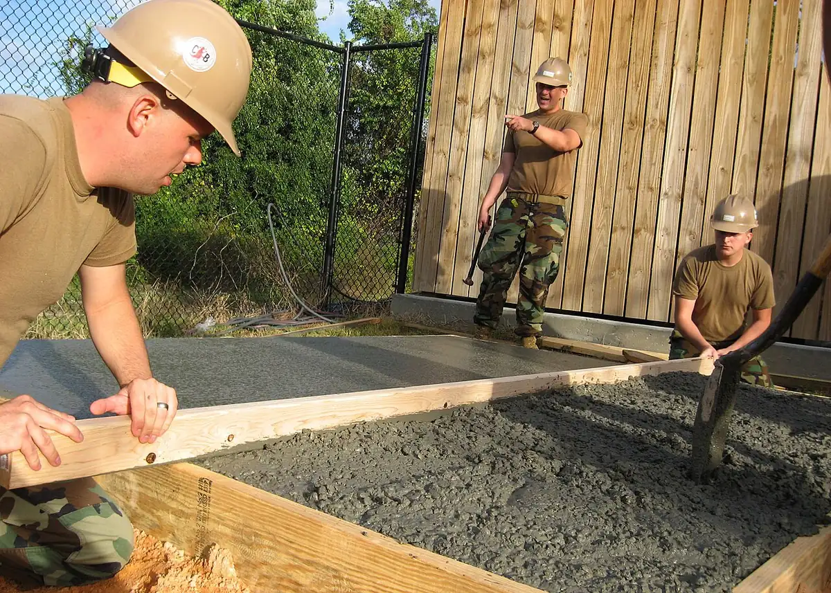 Workers screeding wet concrete inside wood forms for a new slab, as in a pool deck installation