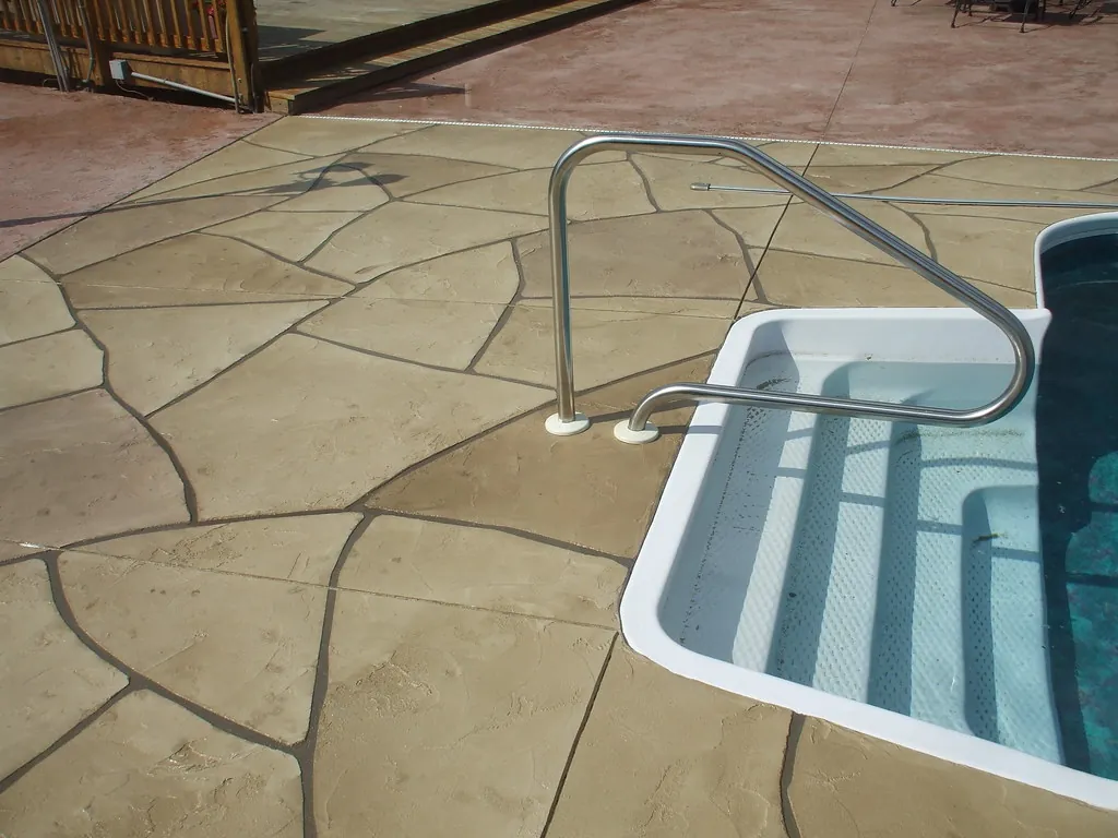 Close view of a stamped concrete pool deck in a random flagstone pattern beside the pool steps